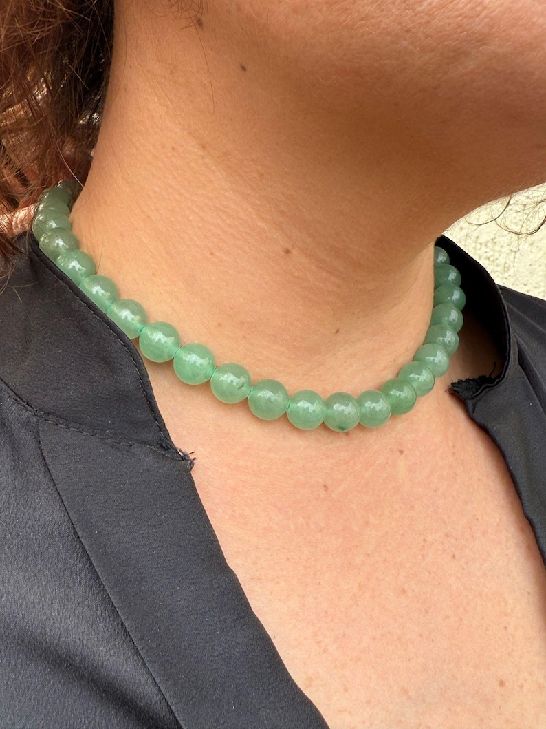 May include: A green jade bead necklace with round beads. The necklace is worn by a person with a black shirt.