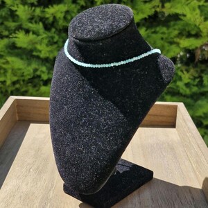 May include: A light blue beaded necklace on a black velvet jewelry display stand.