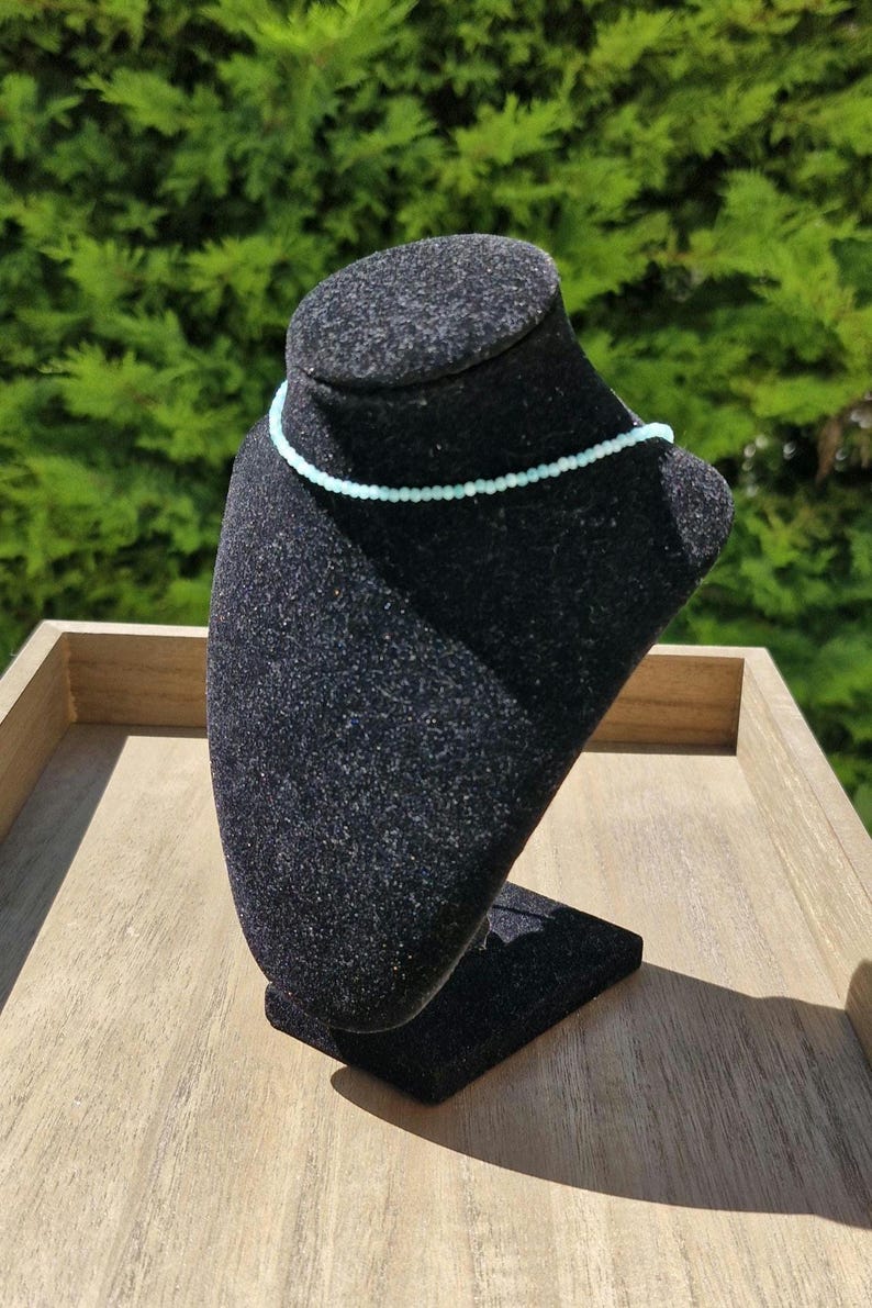 May include: A light blue beaded necklace on a black velvet jewelry display stand.