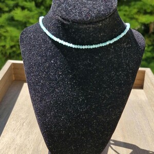May include: A delicate light blue beaded necklace on a black velvet display stand.