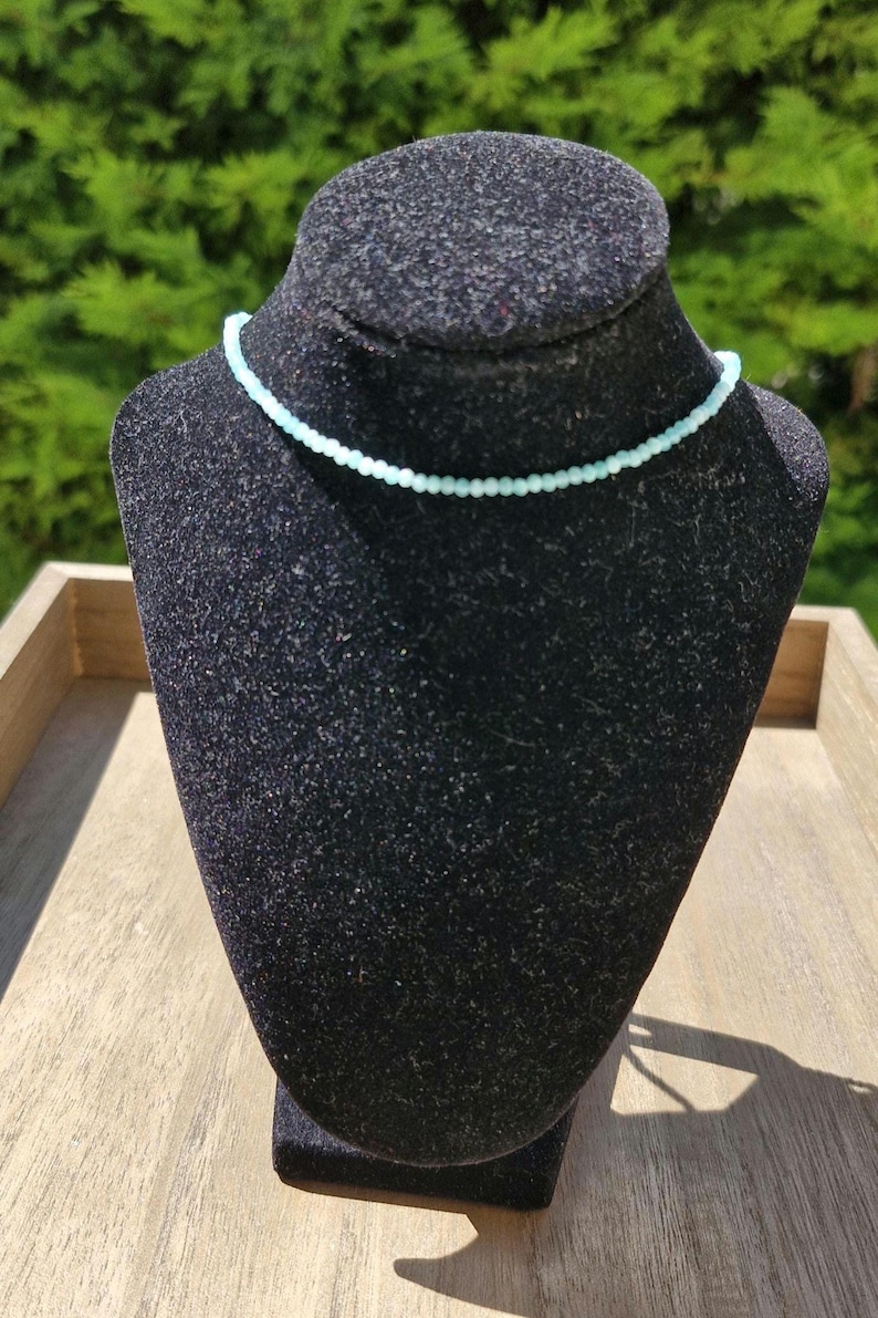 May include: A delicate light blue beaded necklace on a black velvet display stand.