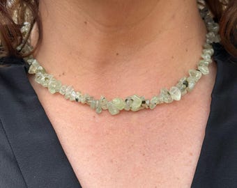 May include: A green gemstone necklace with irregular shaped stones. The necklace is on a person's neck.
