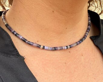 May include: A close-up of a purple, black, and silver beaded necklace. The necklace is made of small, round beads that are strung together on a thin cord.