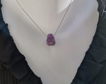 May include: A silver chain necklace with a polished, purple gemstone pendant. The pendant is a rounded rectangle shape and hangs from a delicate chain. The necklace is displayed on a white mannequin bust, with a black top in the background.
