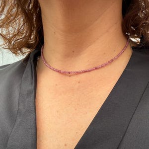 May include: A delicate choker necklace made with small, light purple beads. The necklace is worn by a person with brown hair.