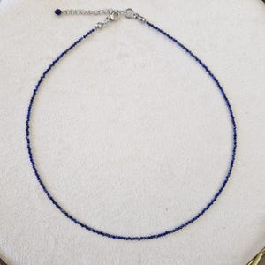 May include: Delicate necklace featuring small, deep blue beads strung together. The necklace has a silver-toned clasp and adjustable chain. The jewelry is displayed on a white surface.
