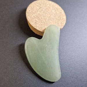 Peut inclure: Un outil de massage facial en jade gua sha en forme de cœur vert clair. L'outil est fait de jade lisse et poli et a un bord arrondi.