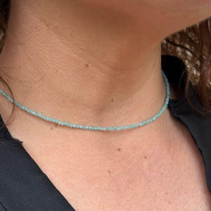 May include: A delicate light blue beaded necklace. The necklace is made of small, round beads and is worn by a person.