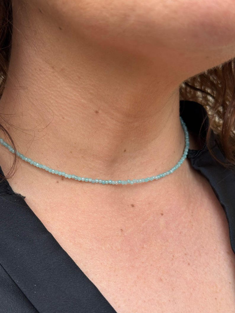 May include: A delicate light blue beaded necklace. The necklace is made of small, round beads and is worn by a person.