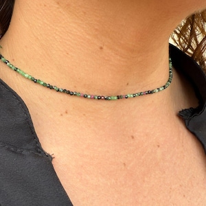 Może przedstawiać: Delikatny naszyjnik choker wykonany z małych czarnych, zielonych i różowych koralików.