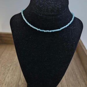 May include: A delicate light blue beaded necklace on a black velvet display stand.