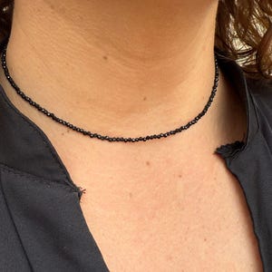 May include: A fine black beaded choker necklace. The necklace features small, dark beads, strung together to form a simple, elegant design. The necklace sits close to the neck, offering a touch of sophistication.