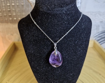 May include: A silver necklace with a teardrop-shaped pendant. The pendant is a translucent purple stone with a silver bail. The necklace is displayed on a black velvet bust against a neutral background.