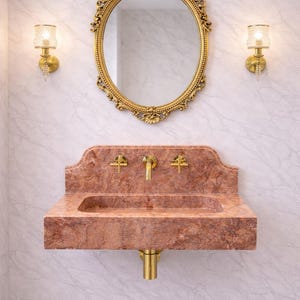May include: A luxurious bathroom vanity set featuring a red marble sink with gold fixtures. Above the sink is a gold-framed oval mirror and two matching sconces. The wall has a marble pattern.