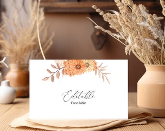 May include: Editable food label with a floral design featuring orange and yellow flowers. The label is on a wooden table with a beige cloth napkin.