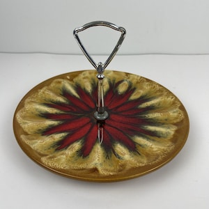 Op de afbeelding: Een serveerschaal met twee niveaus en een decoratief ontwerp. De keramische plaat heeft een rood en bruin bloemmotief met een zilveren metalen handvat. De schaal is rond en geschikt voor het serveren van hapjes of desserts.