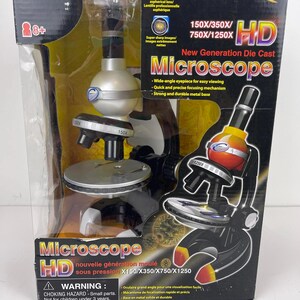 Könnte beinhalten: Ein Mikroskop der neuen Generation in einer Box. Das Mikroskop ist schwarz, silber und gelb. Auf der Box stehen die Worte "Microscope HD" und "150X/350X/750X/1250X". Die Box enthält auch einen Warnhinweis auf Erstickungsgefahr.