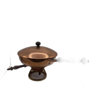 Könnte beinhalten: Ein kupferfarbenes Chafing Dish mit Deckel und kleinem schwarzem Knopf. Das Gericht hat einen runden Sockel mit dekorativem Metalldesign und einem Holzgriff. Das Chafing Dish dient dazu, Speisen warm zu halten.