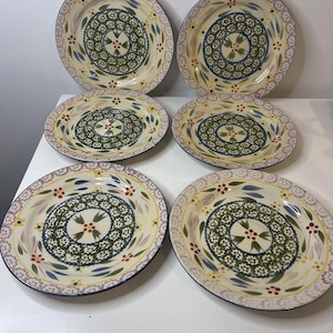 May include: Six ceramic plates with a cream background. Each plate has a central green floral design, surrounded by blue, red, and yellow accents. The rims have a blue border and a decorative floral pattern.