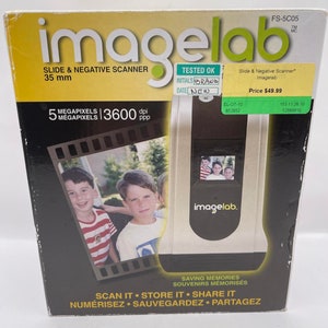 May include: A silver and black Imagelab slide and negative scanner. The box features the text "Slide & Negative Scanner 35 mm" and "5 Megapixels 3600 dpi." The scanner has a small screen displaying a photo. The box also says "Scan it, Store it, Share it."