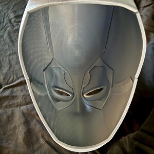 May include: A gray plastic mask with eye holes and a textured surface. The inside of the mask is visible.