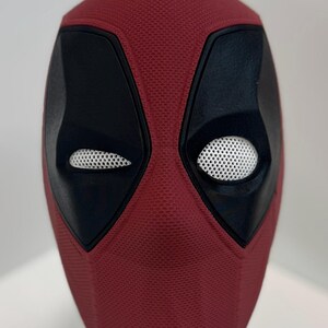 May include: A red and black Deadpool mask with a textured surface and white mesh eye holes.