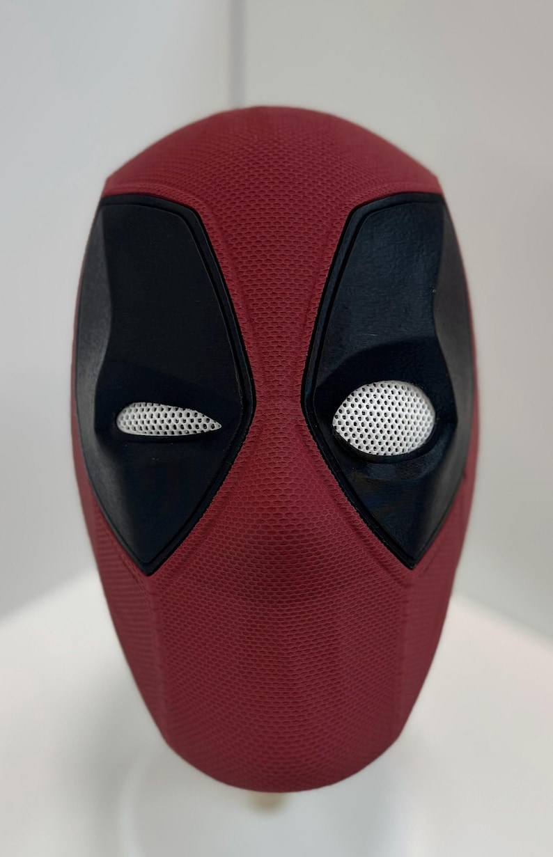 May include: A red and black Deadpool mask with a textured surface and white mesh eye holes.