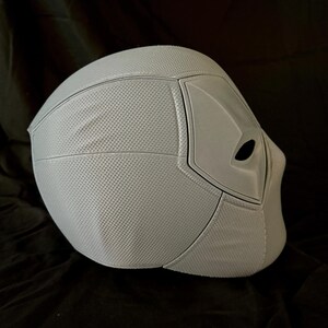 May include: A white plastic Deadpool mask with a textured surface. The mask has a black eye hole and a black outline around the eye hole.