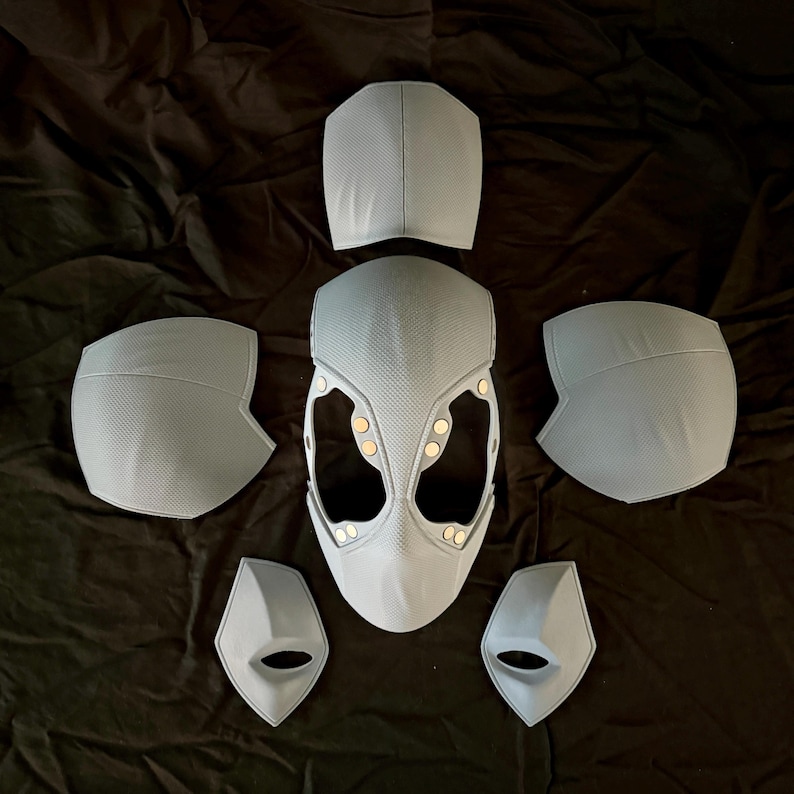 May include: A set of six white plastic costume pieces, including a helmet, two shoulder pads, two forearm guards, and a chest piece. The pieces are all textured and have a slightly metallic sheen.