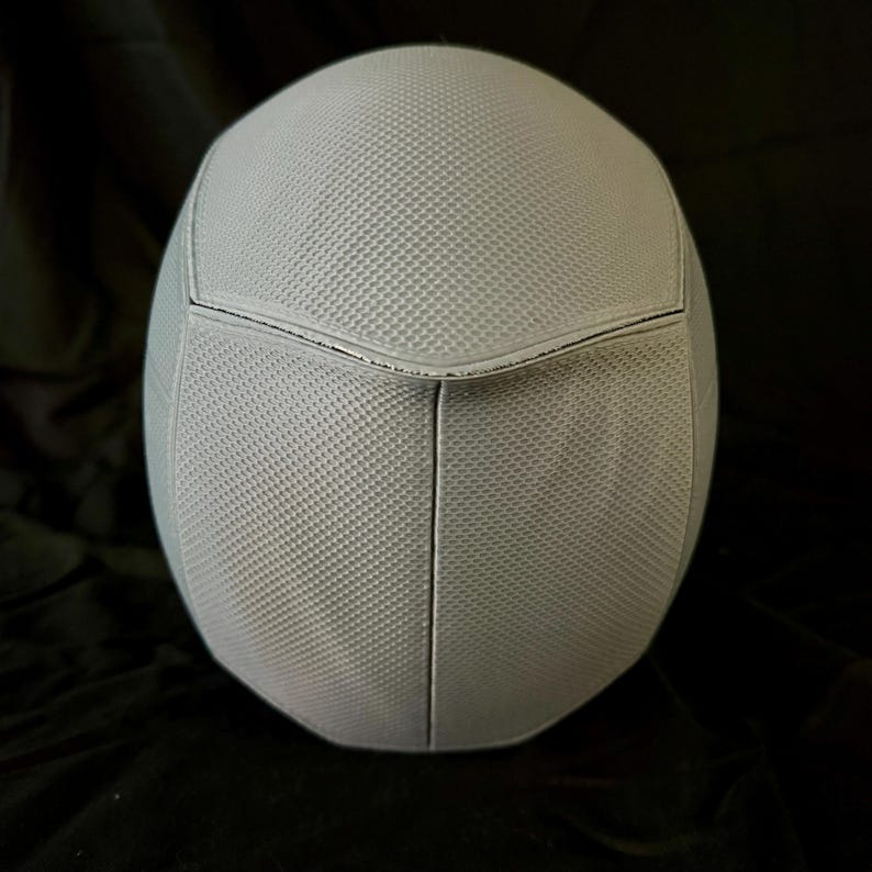 May include: A white helmet with a textured surface and a seam down the center.