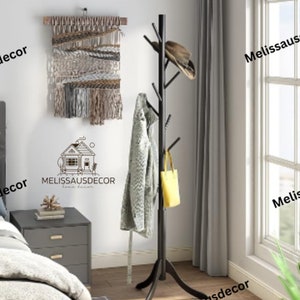May include: Black metal coat rack with a tree branch design. The rack has multiple hooks for hanging coats, hats, and bags. A gray sweater and a yellow bag are hanging on the rack. A brown woven wall hanging is on the wall behind the rack.