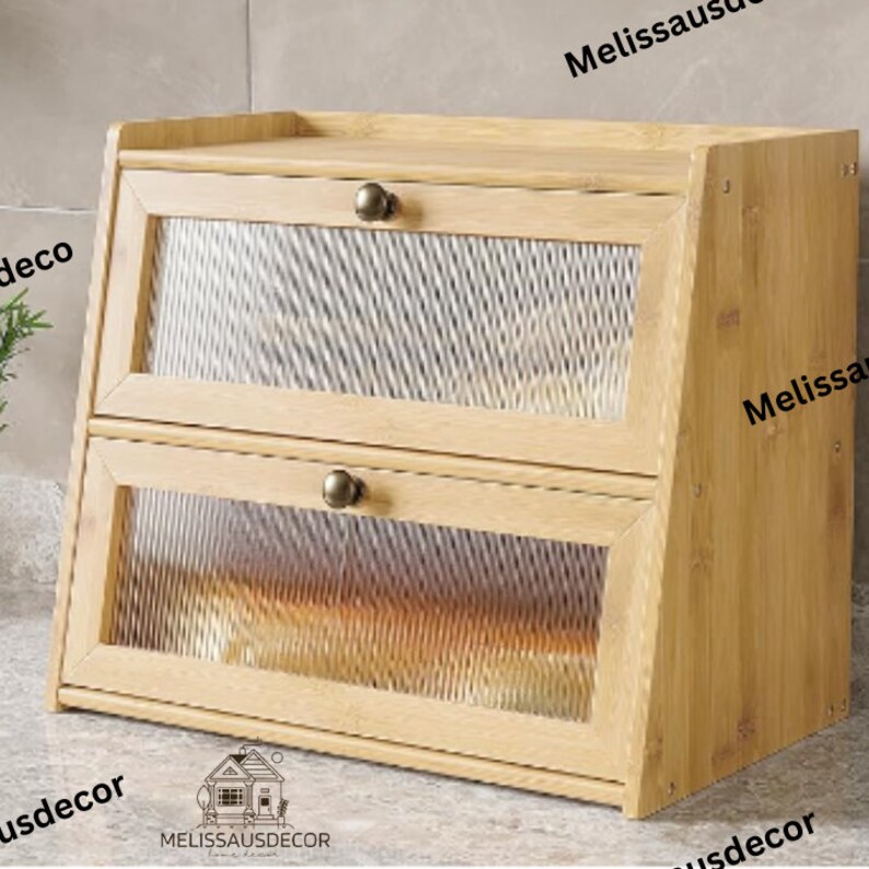 May include: A two-tiered wooden bread box with a clear, textured plastic front. The bread box has a light brown wood finish and two metal handles.