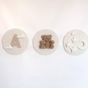 以下が含まれることがあります： 白い丸いふわふわのフェルト製の壁飾り3つ。最初の飾りは、茶色のフェルト製のアルファベットAと白いフェルト製の雲2つ。2つ目の飾りは、茶色のフェルト製のテディベア。3つ目の飾りは、白いフェルト製の三日月と白いフェルト製の星5つ。