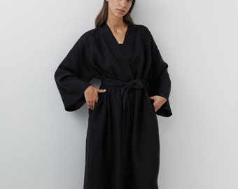 May include: A black linen robe with a long, flowing silhouette and a tie belt. The robe has a V-neckline and long sleeves.