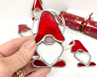 May include: A set of four stained glass Christmas ornaments shaped like gnomes. The gnomes are red and white with silver trim.