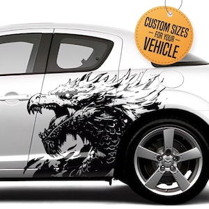 May include: A white car with a black and white dragon graphic decal on the side. The decal is of a dragon with its mouth open and its wings spread. The decal is on the side of the car, just behind the front wheel. The car is a sports car with a low profile and a sleek design. The decal is a great way to add a unique and stylish touch to any car.  "Custom Sizes for your Vehicle" is written on a yellow tag.