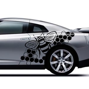 May include: Silver sports car with a black and white bee and honeycomb graphic on the side. The car has black wheels and a spoiler. The background is white.