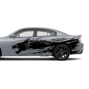 May include: A silver sedan with black wheels and a black dragon graphic on the side. The dragon design is a stylized, brushstroke-style illustration, adding a dynamic and artistic element to the vehicle's appearance.