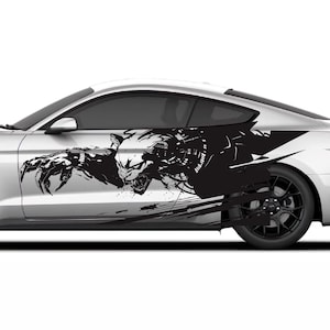 May include: A silver sports car with black wheels and a black graphic design on the side. The graphic appears to be a stylized skull and claw design. The car is set against a white background.