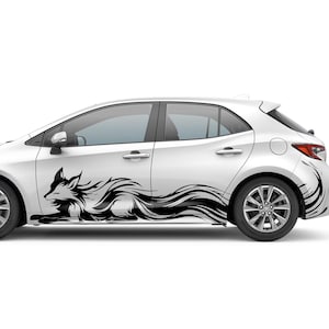 May include: White hatchback car with a black fox decal on the side. The decal features a stylized fox with flowing lines, creating a dynamic and artistic design. The car has black wheels and tinted windows.