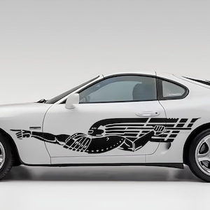 May include: White sports car with a black graphic of a person pointing forward. The car has silver rims and a rear spoiler. The car's design is sleek and modern.