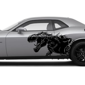 Op de afbeelding: Zilveren coupé met zwarte wielen en een zwarte dinosaurusafbeelding op de zijkant. De auto heeft een spoiler en getinte ramen. De dinosaurusafbeelding is een gedetailleerd silhouet.