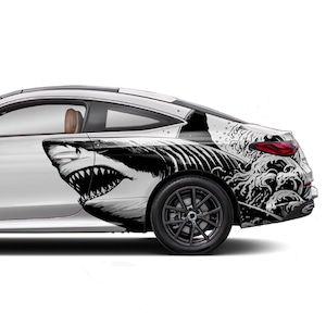 May include: A white car with a black and white shark and wave graphic decal on the side. The decal features a shark with an open mouth and waves crashing behind it.
