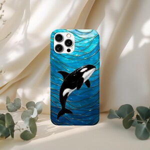 May include: A phone case with a black and white orca design swimming in a blue ocean. The case has a glossy finish and a protective design. The orca is the focal point, set against a background of blue and gold lines.