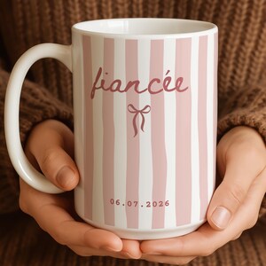 Fiancée mug in blush pink stripes with bow design and custom date, held in hands