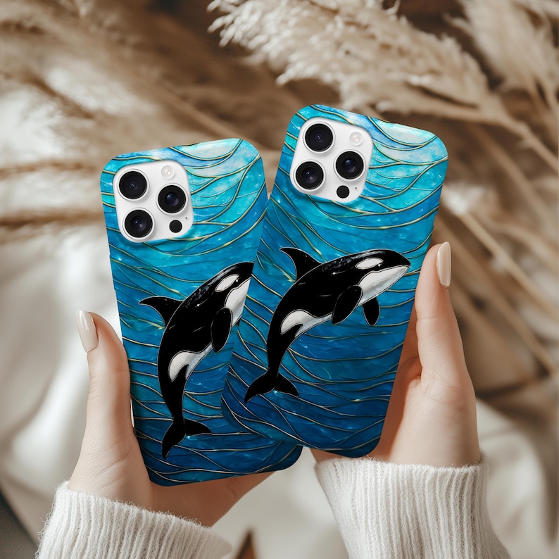 May include: Two phone cases featuring a blue and gold abstract pattern and a black and white orca whale illustration. The cases are held up against a neutral backdrop.