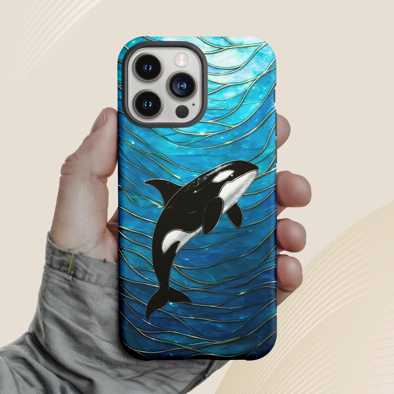 May include: A smartphone case featuring a black and white orca whale design against a blue background with gold accents. The case has a glossy finish and a wave pattern. The case is designed to fit a smartphone.