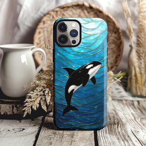 May include: A smartphone case with a black and white orca whale design. The case has a blue background with gold-coloured wavy lines. The orca is swimming in the water. The case is designed to fit a mobile phone.