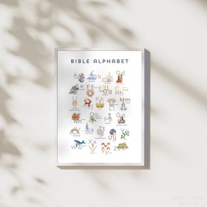 May include: A framed print titled "BIBLE ALPHABET" features an illustrated alphabet with religious themes. Each letter is paired with a watercolor image, such as a church, rainbow, and whale. The print is in a white frame.