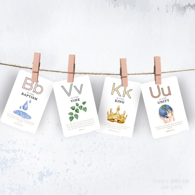 May include: Four white cards with letters B, V, K, and U, each clipped to a string with wooden clothespins. The cards feature watercolor illustrations and text: "Baptism," "Vine," "King," and "Unity." The cards are suspended against a light background.